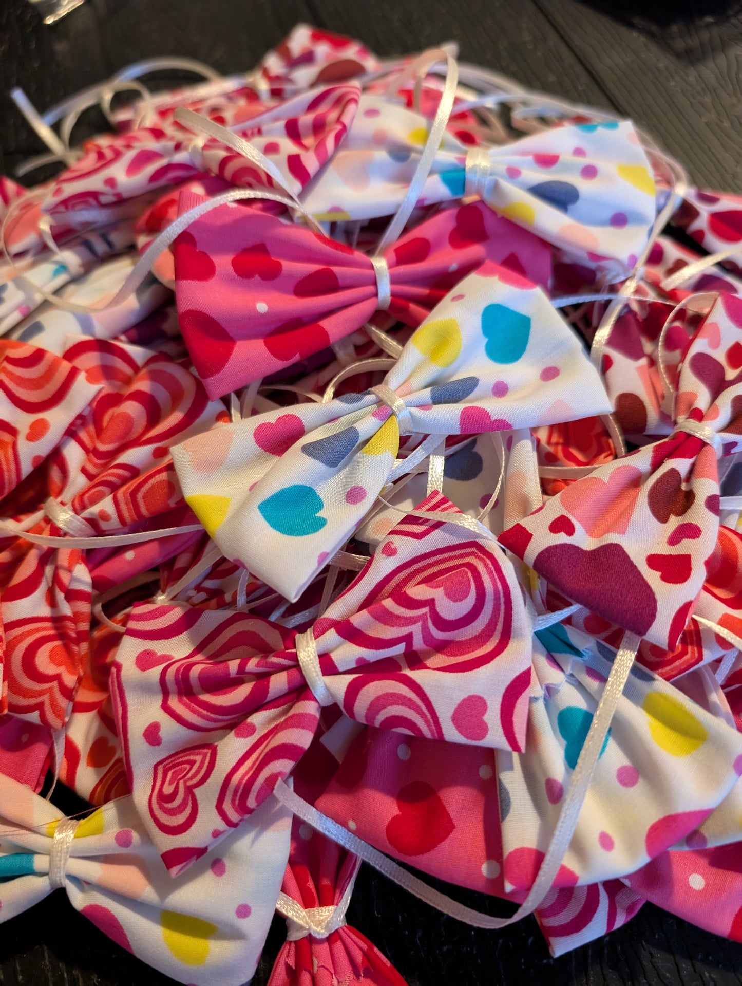 Collection of colorful dog bows with heart patterns on a dark surface